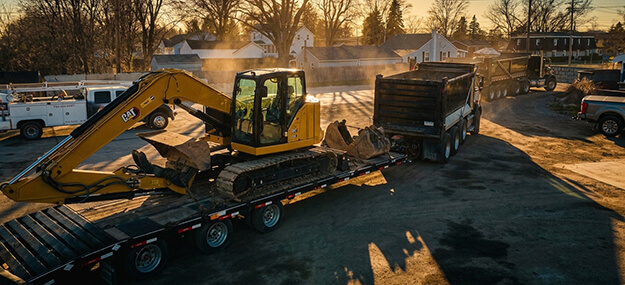 Excavator being loaded onto trailer for transport during construction hauling operation