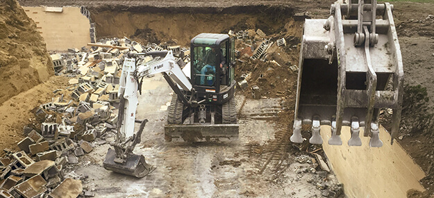 Excavator performing foundation demolition and structure removal during site clearing process