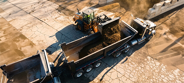 Loader filling dump truck with material during construction hauling and sitework operation