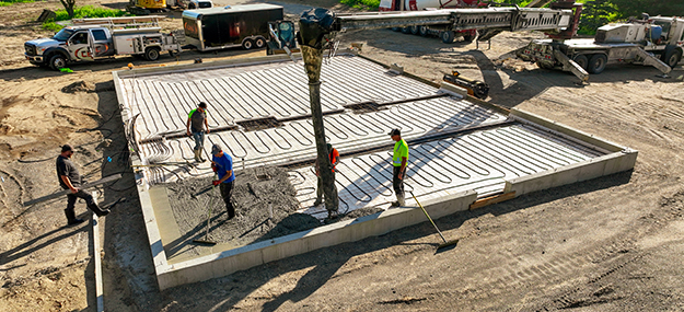 Crew pouring and finishing concrete slab for pole barn foundation during installation