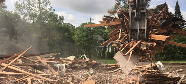 Excavator removing wood debris during residential demolition and site clearing process